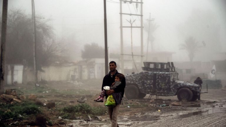 An Iraqi man carries his child as they flee west Mosul