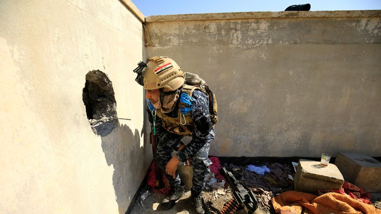 An Iraqi policeman looks through a hole blasted in a wall where IS fighters were hiding