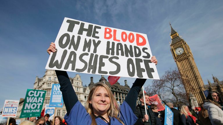 A protester, an NHS doctor, holds a placard up in front of the Elizabeth Tower, also known as Big Ben at the Houses of Parliament during a march against private companies&#39; involvement in the National Health Service (NHS) and social care services provision and against cuts to NHS funding in central London on March 4, 2017