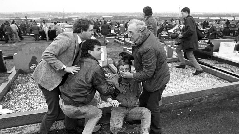 McGuinness assists an injured man at Milltown Cemetary, Belfast, after an attack at the funerals of three IRA members killed in Gibraltar, 1988