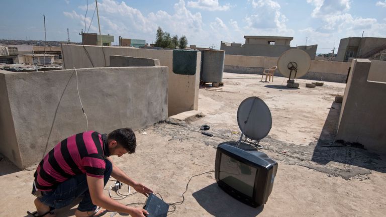 A man installs a satellite dish on the rooftop of a house in eastern Mosul