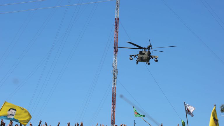 Kurds wave flags as a medical helicopter, from the US-led coalition, flies over the site of Turkish airstrikes near northeastern Syrian Kurdish town of Derik, known as al-Malikiyah in Arabic, on April 25, 2017