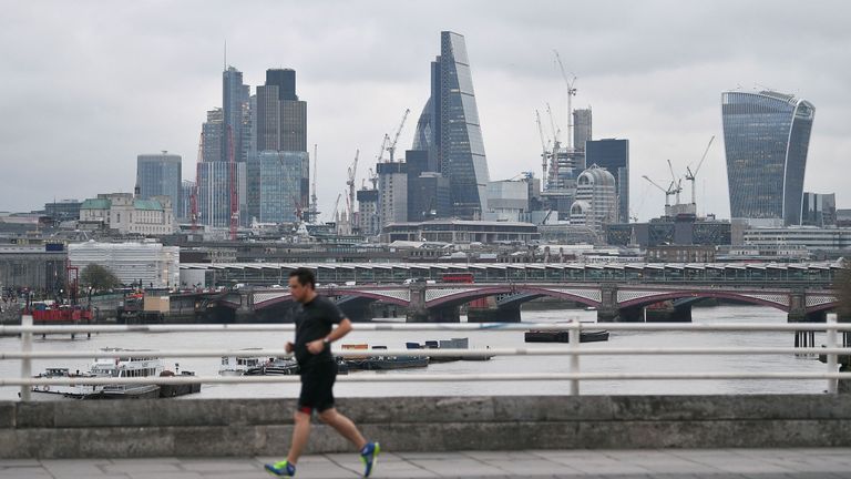 A jogger runs across a bridge spanning the River Thames as skyscrapers in the City of London are pictured om the horizon in London on March 29, 2017