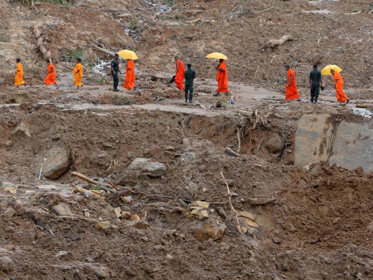 Buddhist monks cross a landslide as rescue workers search for survivors in Athweltota