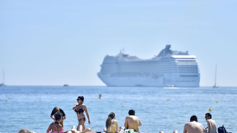 A cruise liner is anchored off shore as people enjoy the beach 