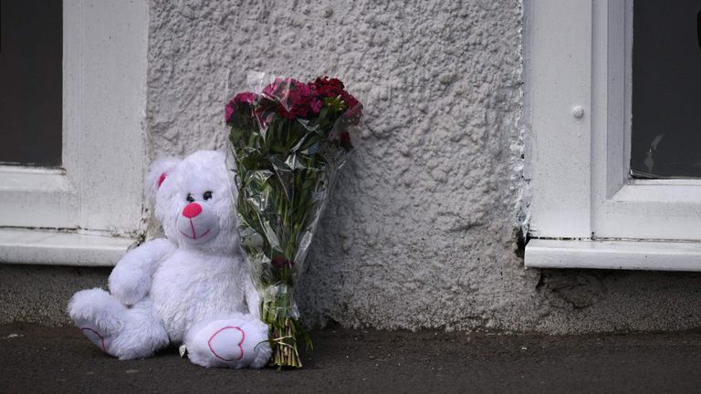 A floral tribute and a teddy bear are left by police tape near the venue