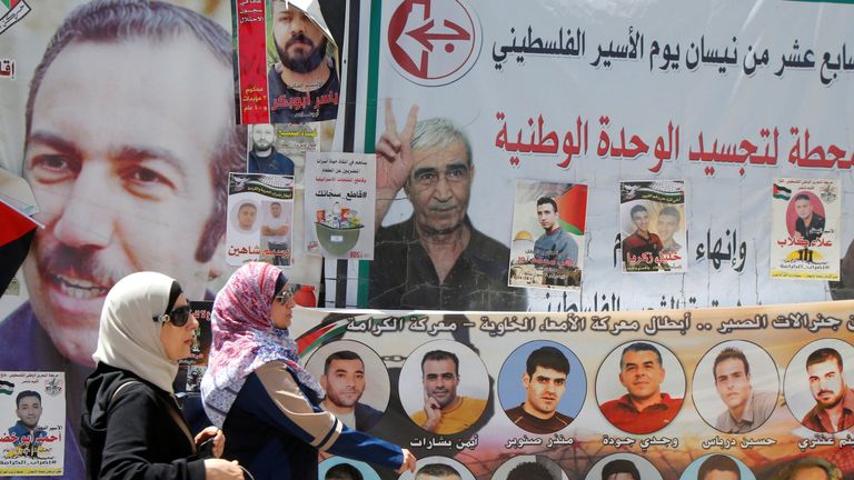 Women walk past images of Palestinian prisoners on hunger strike in Israeli jails