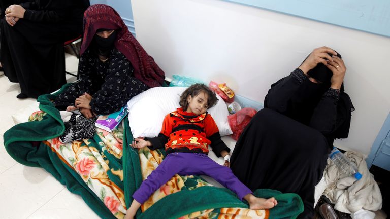 A mother holds her heads in her hands as she sits next to a young girl with cholera in Sanaa, Yemen