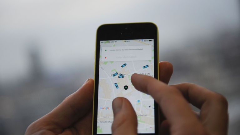 A man poses holding a smartphone showing the app for ride-sharing cab service Uber in London