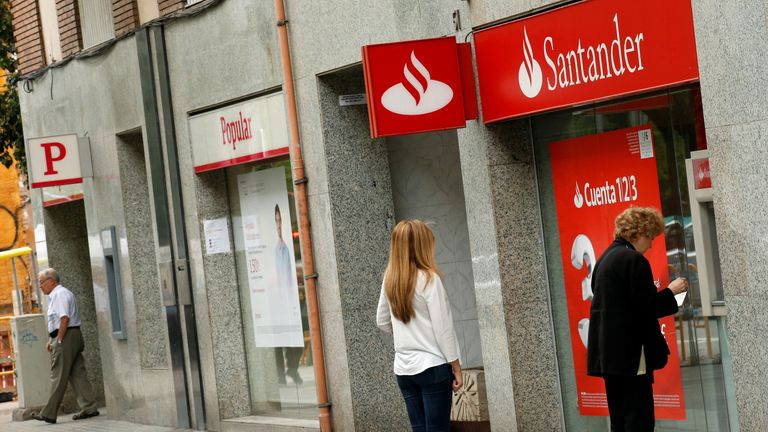 People use a Santander's cash dispenser (ATM) as a man leaves a Banco Popular office in Barcelona