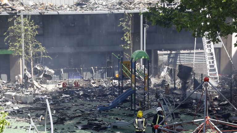 Firefighters stand amid debris in a playground under Grenfell Tower