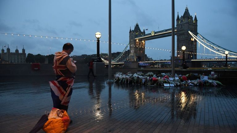 A man stands near flowers layed at Potters Fields Park in London