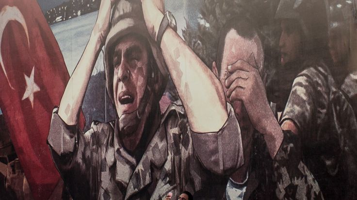A man takes a photograph in front of a large billboard displaying a painted poster depicting the events of the July 15, 2016 coup attempt