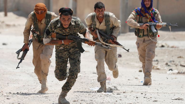 Kurdish fighters from the People&#39;s Protection Units (YPG) run across a street in Raqqa