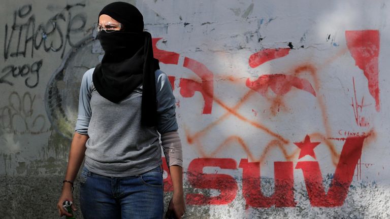 A demonstrator stands next to a graffiti depicting the eyes of Venezuela's late President Hugo Chavez as she holds Molotov cocktails 