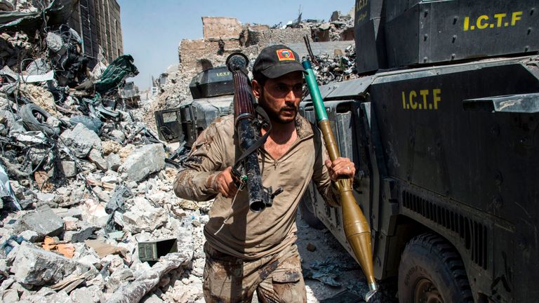 A member of the Iraqi forces walks through the rubble past humvees as he carries a rocket-propelled grenade and launcher 