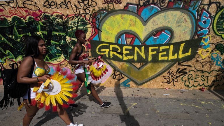 Performers walk past graffiti marking the Grenfell tragedy