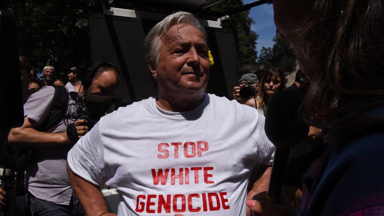 A free speech rally participant wearing a "stop white genocide" t-shirt speaks with a reporter outside...
