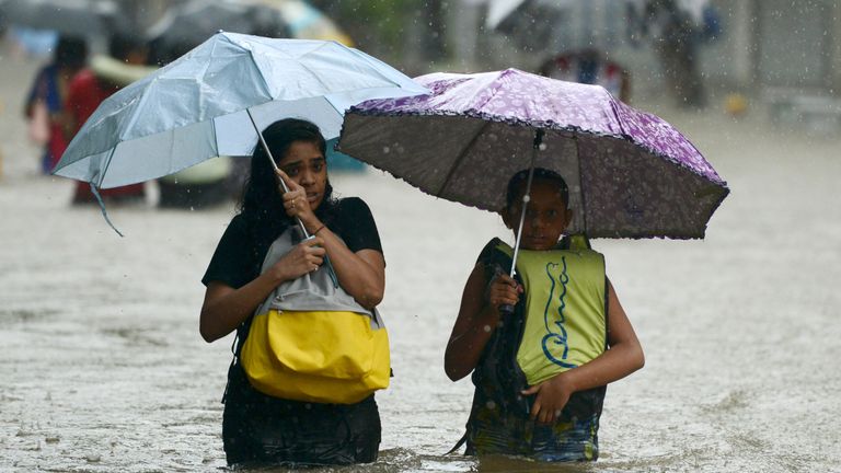 Indian girls wade through a flooded street during heavy rain in Mumbai