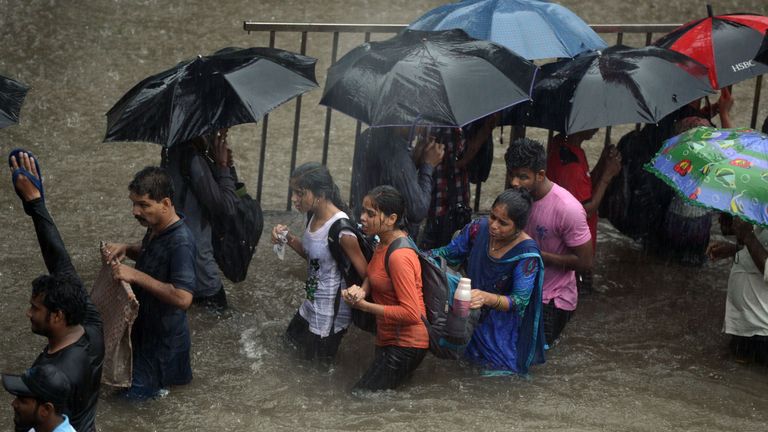 People walk along a flooded street during heavy rain showers in Mumbai