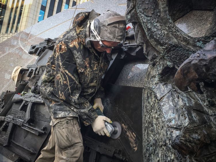 A worker uses an angle grinder to remove the StG 44 drawing