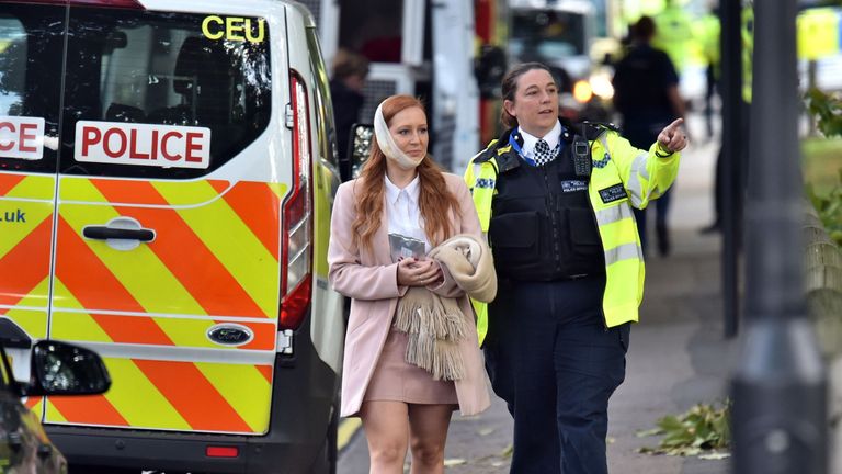 An injured woman is assisted by a police officer close to Parsons Green station 