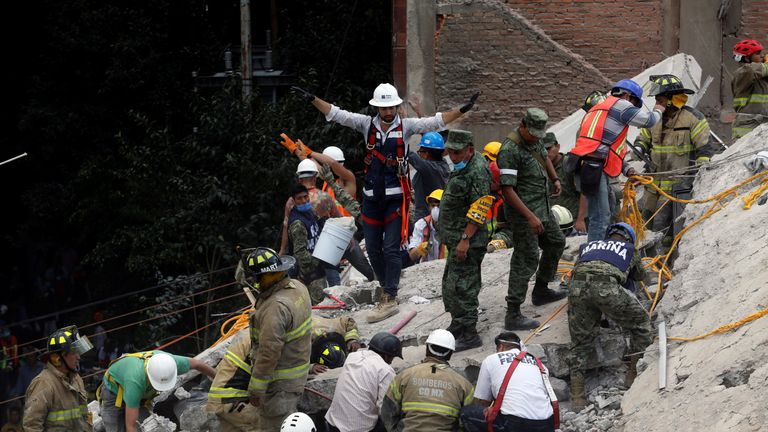A rescue worker motions for everybody to be quiet as they search for people under the rubble 