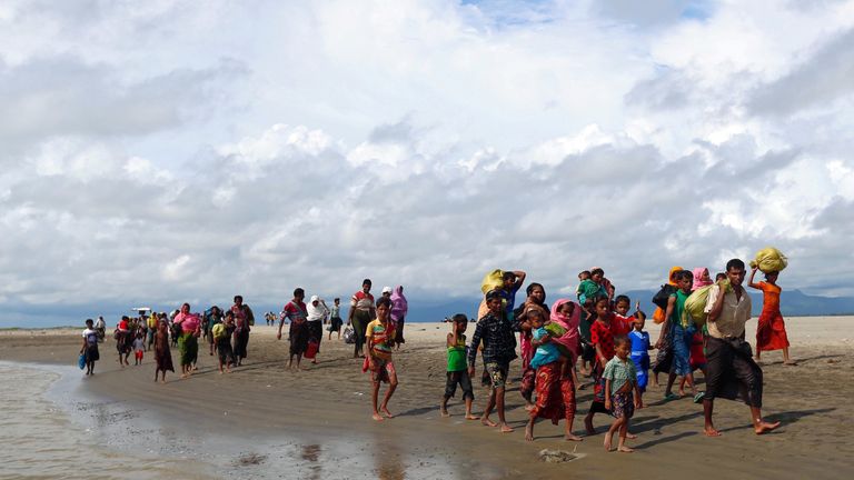 Rohingya refugees walk on the shore after crossing the Bangladesh-Myanmar border by boat through the Bay of Bengal
