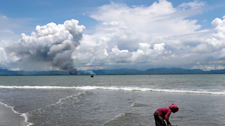Smoke is seen on Myanmar&#39;s side of border as a Rohingya refugee woman cleans her shoes after crossing the Bangladesh-Myanmar border