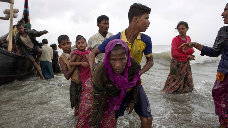 A Rohingya man helps an elderly woman out of the water after arriving in Dakhinpara, Bangladesh