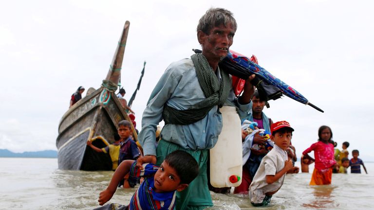 A Rohingya refugee man pulls a child to the shore after crossing the Bangladesh-Myanmar border by boat through the Bay of Bengal in Shah Porir Dwip