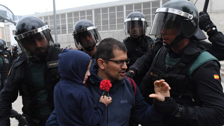 Police take hold of a man and a child holding a red flower 