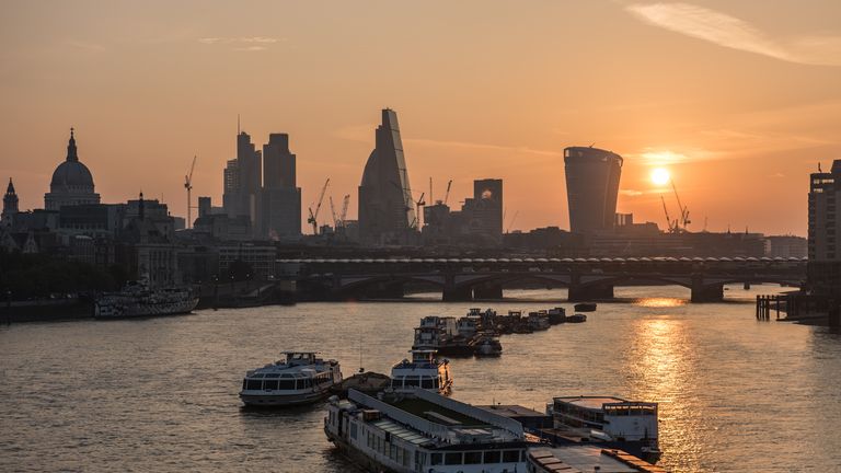 The sun rises over the City of London seen from Waterloo Bridge. Boats moored in the river Thames. The skyline includes St Paul&#39;s Cathedral, skyscrapers of The City including The Gherkin, the Cheesegrater, 20 Fenchurch Street &#39;Walki-Talkie&#39;