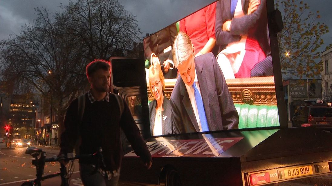 Man walking by Sky News lorry with budget on the screen.