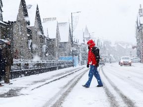 A pedestrian walks through the snow as he crosses the road during a snowfall in Pitlochry, Scotland November 24, 2017