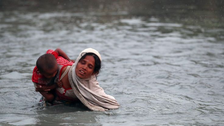 A Rohingya refugee carries a child across the Naf River as they cross in to Bangladesh