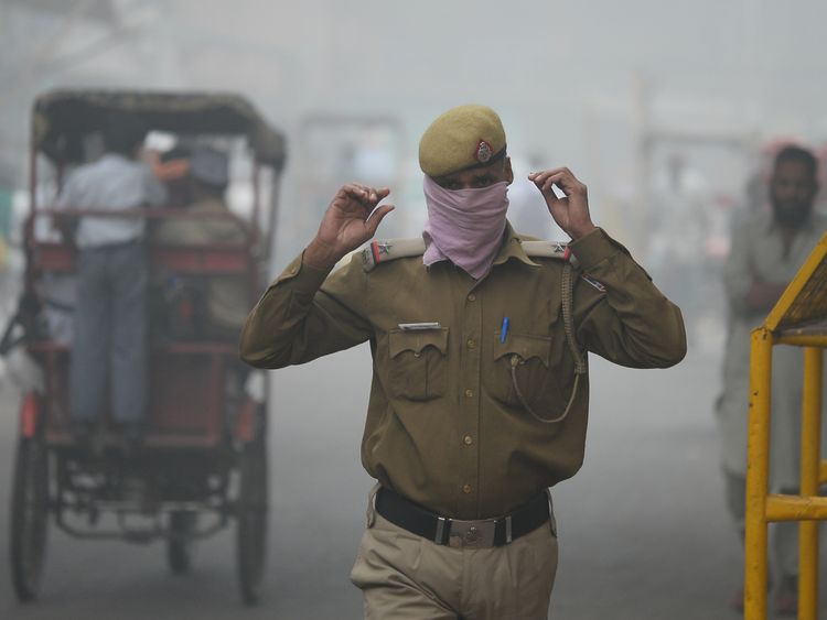 An Indian policeman covers his face with handkerchief as he walks in the smog