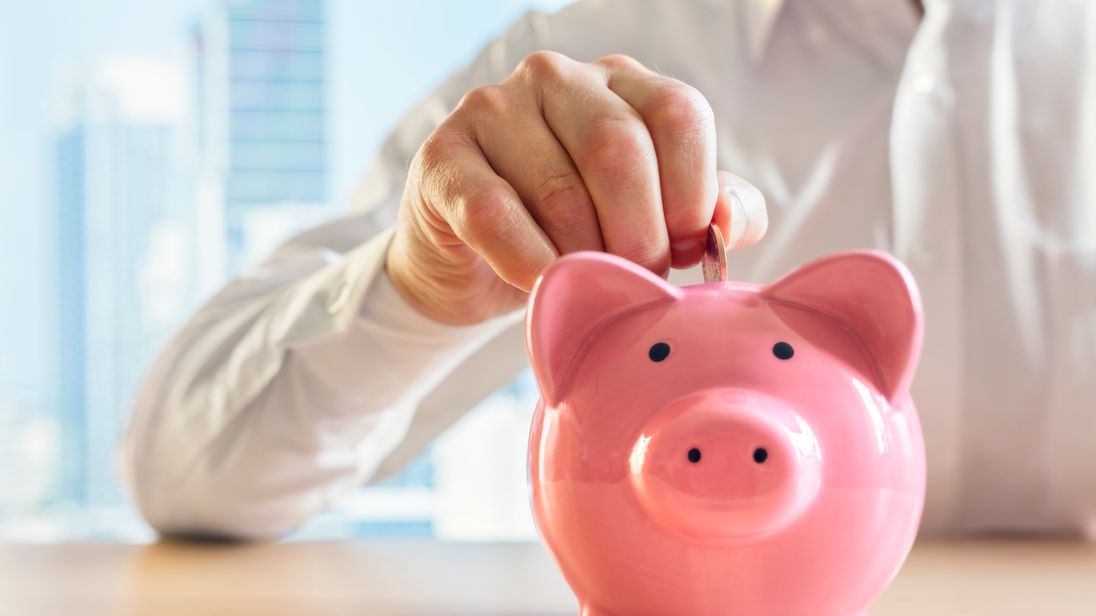 Man putting a coin into a pink piggy bank concept for savings and finance