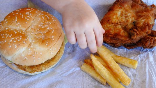 A young girls eats a chicken burger, French fries and fried chicken.