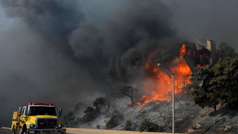 A fire crew passes a burning home during a wind-driven wildfire in Ventura, California