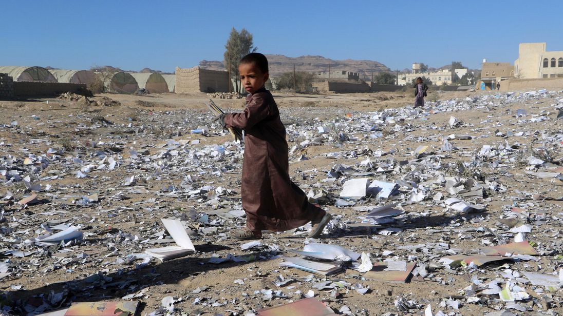 A boy holds a book as he walks on books scattered on the ground after an air strike hit a school book storage building in the northwestern city of Saada Yemen