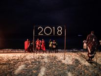 People wait for a moment to light a sign that reads 2018 during the New Year's Eve celebration on Nungwi Beach in Zanzibar, Tanzania, on December 31, 2017. / AFP PHOTO / GULSHAN KHAN (Photo credit should read GULSHAN KHAN/AFP/Getty Images)