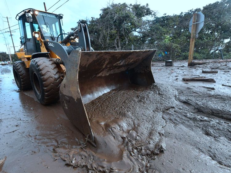 A bulldozer clears mud off the road near a flooded section of US 101 freeway in Montecito, California