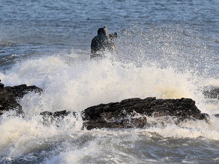 A man taking photographs gets caught by crashing waves at High Rock in Portmarnock, Dublin