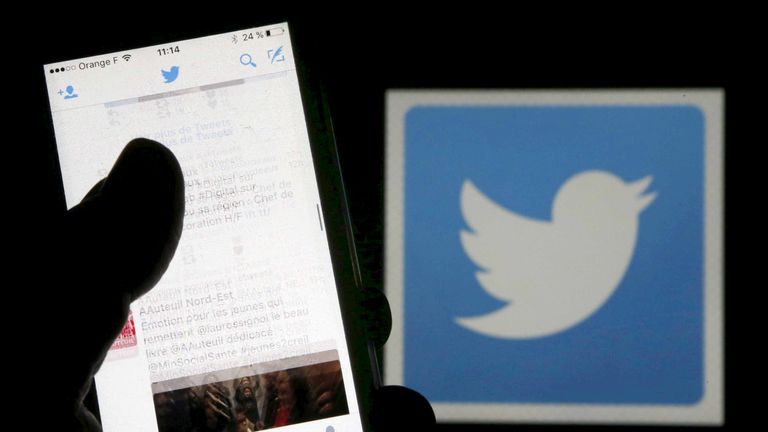 A man reads tweets on his phone in front of a displayed Twitter logo