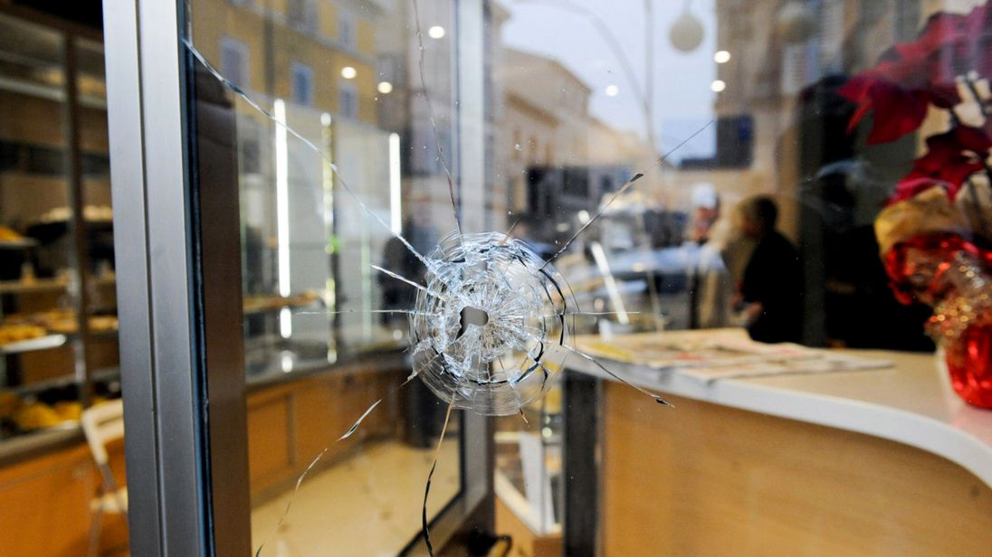 A bullet hole is seen in a shop window as police forensics officers carry out investigations in the area following the wounding of several foreign nationals in a drive-by shooting at Macerata, on February 3, 2018