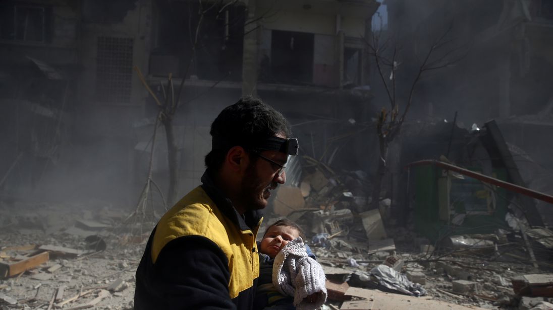 A baby is carried away from the remains of a bombed out building