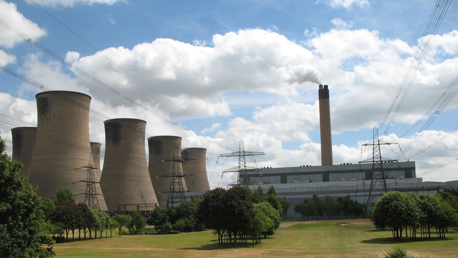 Image shows a large coal fired power station. On the left a group of concrete cooling towers, on the right a large flat roofed building with a tall chimney rising from its centre section.
