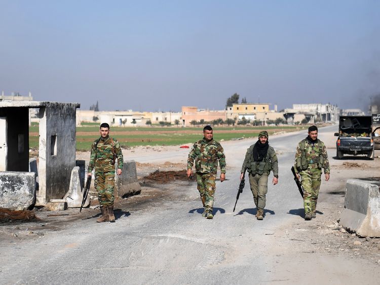 Syrian government forces walk past an abandoned checkpoint in Abu al-Duhur