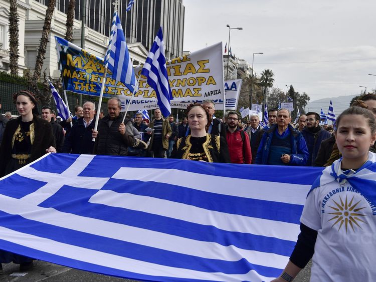 A girl (R) wears a tee-shirt bearing the Vergina Sun, adopted by Greek Macedonians as a symbol of Greek Macedonia, as she holds a flag of Greece during a demonstration to urge the government not to compromise in the festering name row with neighbouring Macedonia, in front of the parliament of Greece, located in the Old Royal Palace (background), at the Syntagma Square in Athens, on February 4, 2018